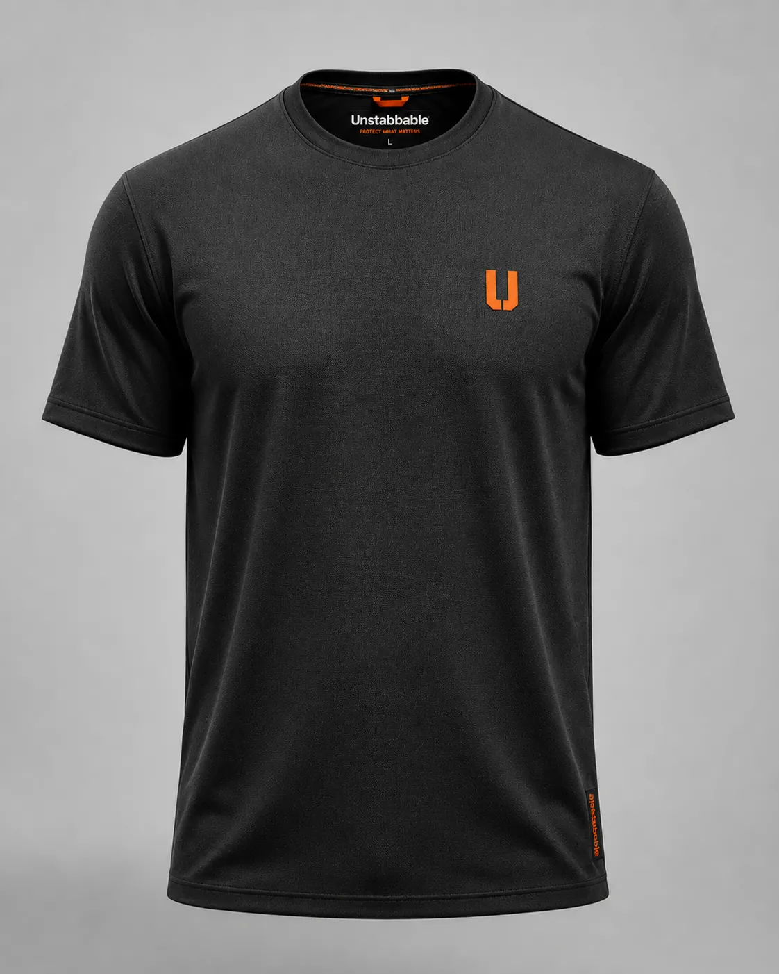 The matte black unstabbable t-shirt on an invisible mannequin against a light grey studio background, with a small safety-orange logo on the chest.